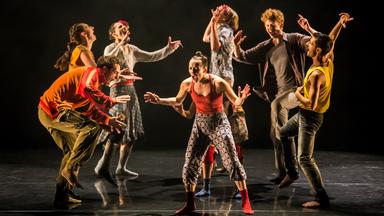 "Gauthier Dance - SWAN LAKES": Mehrere Tänzer*innen, in bunter Straßenkleidung stehen auf der Bühne. Sie bewegen sich rhythmisch und singen.