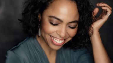 Eine junge Frau lacht mit geschlossenen Augen in die Kamera