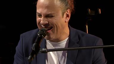 Ein Mann singt in ein Mikrofon, während er Klavier spielt.