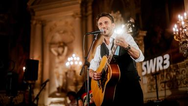 Sänger vor einem Hintergrund mit Kerzen und Stuckdecke