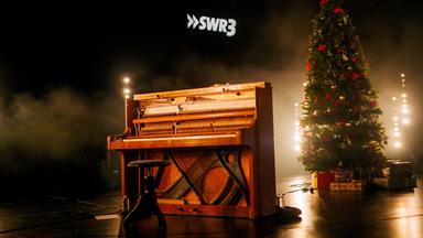 Ein Klavier auf einer Bühne vor einem großen Weihnachtsbaum.