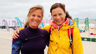 Zwei Frauen stehen Arm in Arm vor einem Strand mit Strandkörben.