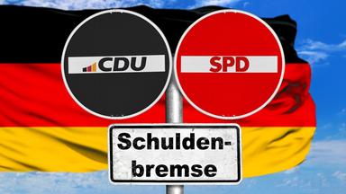 An einem Metallpfahl sind zwei runde Schilder befestigt, auf denen CDU und SPD steht. Darunter hängt ein Schild mit der Aufschrift Schuldenbremse. Hinter den Schildern weht eine Deutschlandflagge.