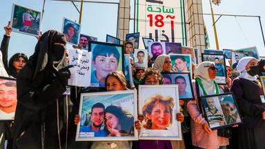 Frauen mit Kopftüchern und teils mit verhülltem Gesicht, sowie Kinder halten Fotos von vermissten Familienmitgliedern hoch.