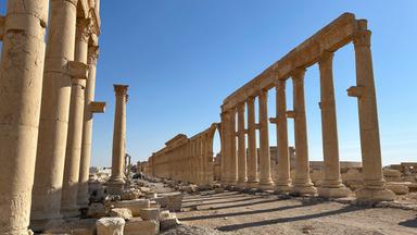 antike Säulen stehen vor blauem Himmel im Wüstensand.