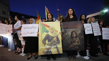 Mehrere Menschen halten Banner und Plakate bei einer Demonstration im Dunkeln.