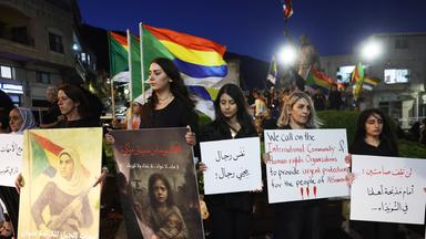 Mehrere Menschen halten Banner und Plakate bei einer Demonstration im Dunkeln.