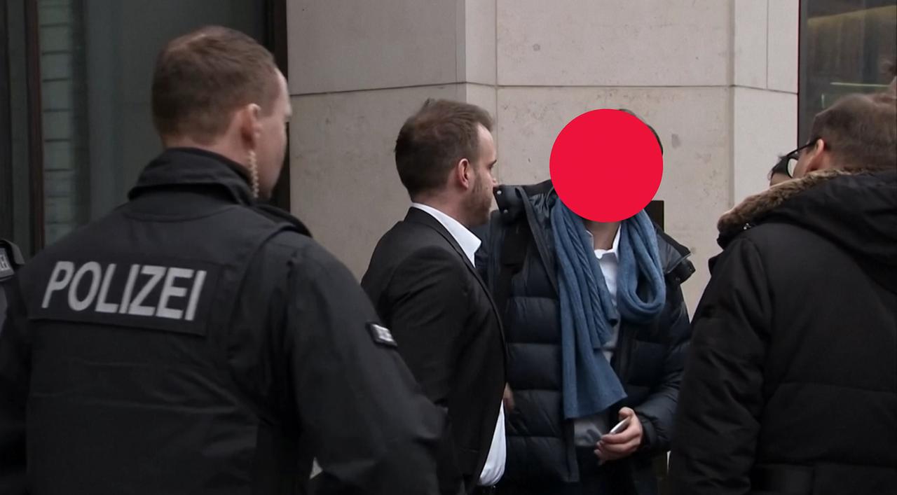 Mehrere Männer, darunter im Vordergrund einer auf dessen Jacke "Polizei" steht, umringen einen Mann, der abgeführt wird. Sein Gesicht ist aus Gründen des Persönlichkeitsschutzes unkenntlich gemacht.