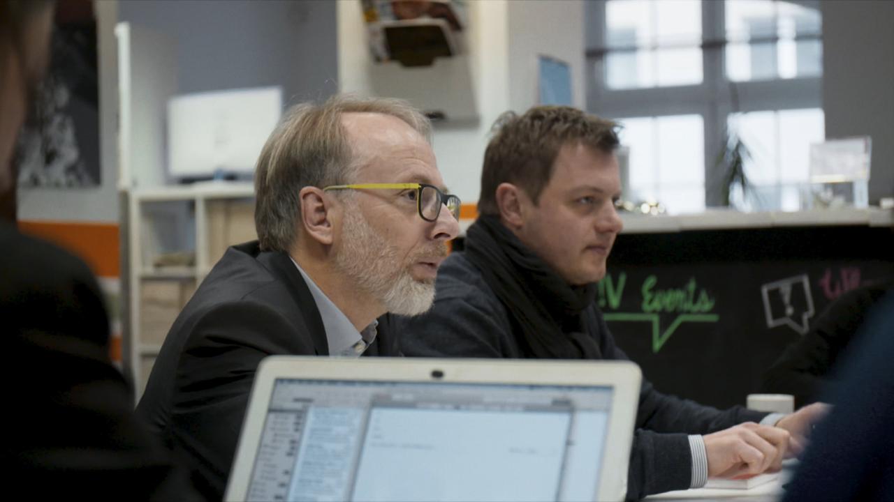 Die Journalisten Oliver Schröm und Christian Salewski sitzen an einem Konferenztisch im Gespräch. Im Vordergrund steht der Bildschirm eines Laptops.