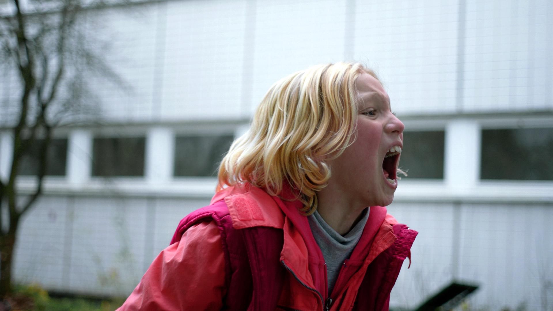 Ein junges Mädchen mit blonden Haaren schreit auf der Straße.