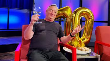 Ein Mann sitzt mit Weinglas in der Hand vor einer goldenen Zahl.