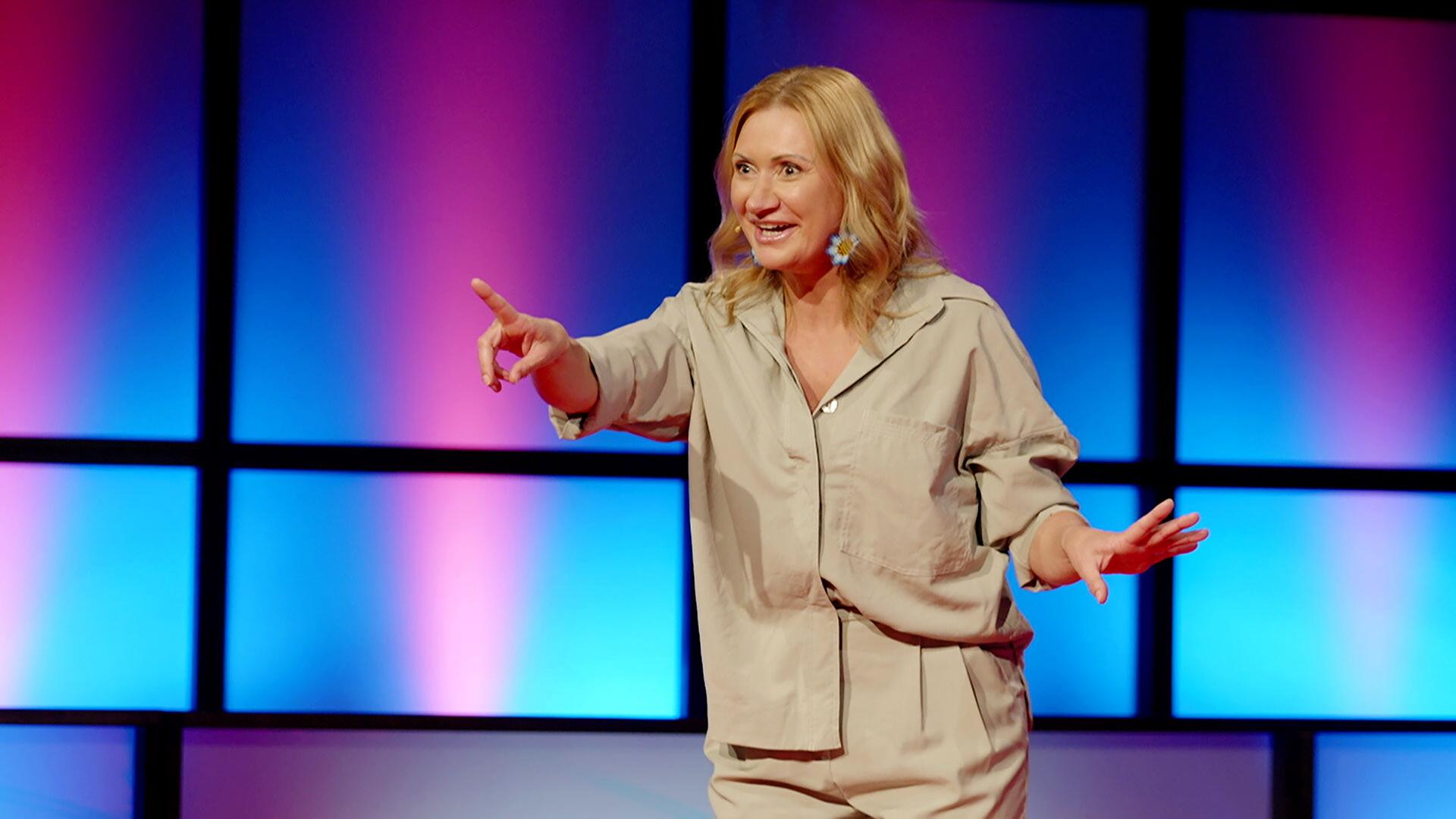 Eine Frau steht vor einer lila-blauen Bühnendeko.