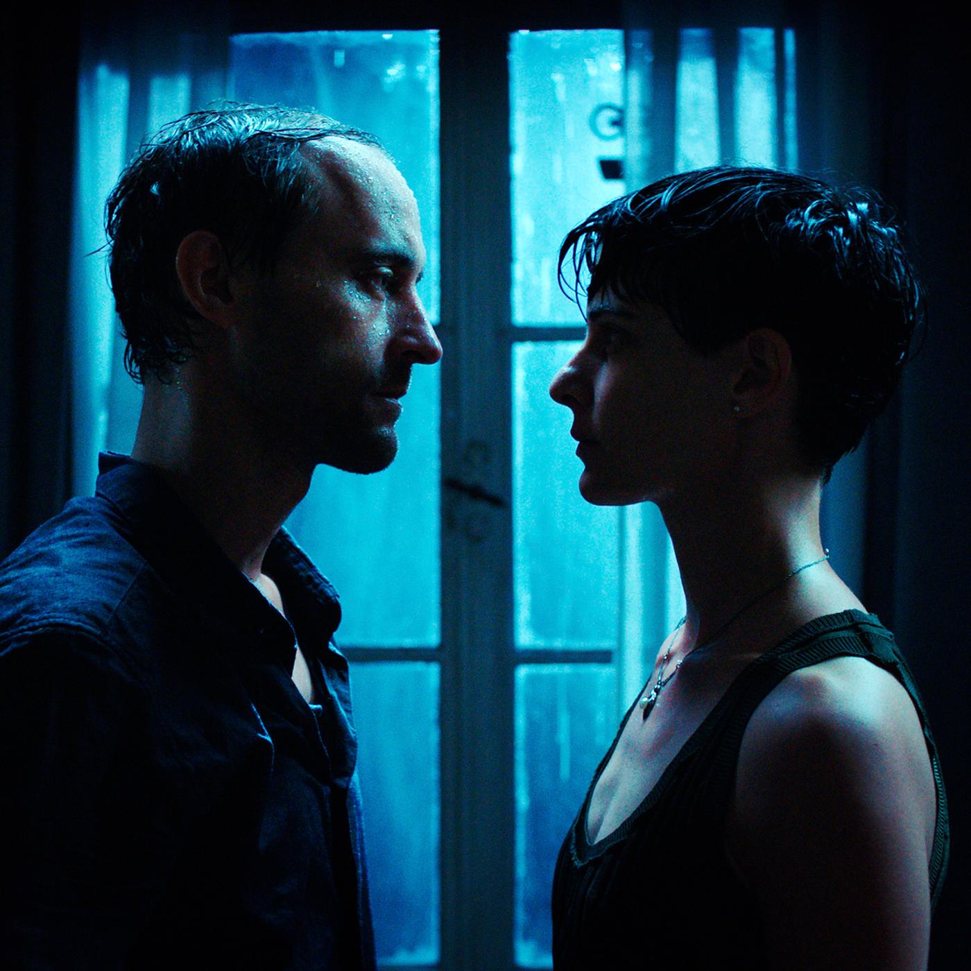 Ein Mann und eine Frau stehen vor einem Fenster mit bläulichem Licht und schauen sich ernst an