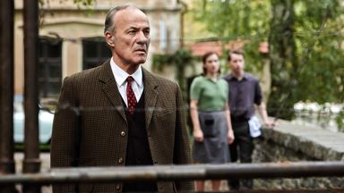 "TANNBACH - Schicksal eines Dorfes (5): Frieden aus Stein": Georg von Striesow (Heiner Lauterbach) steht auf einer kleinen Steinbrücke und blickt fassungslos auf den Stacheldraht-Zaun vor sich.