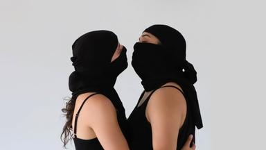 "Tanz aus Israel": Zwei Tänzerinnen umarmen sich.  Sie tragen eine schwarzes Tuch vor dem Gesicht. Nur die Augen sind zu erkennen. Bekleidet sind sie mit einem schwarzen Top.