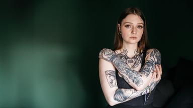 Lea blickt mit verschränkten Armen in die Kamera.