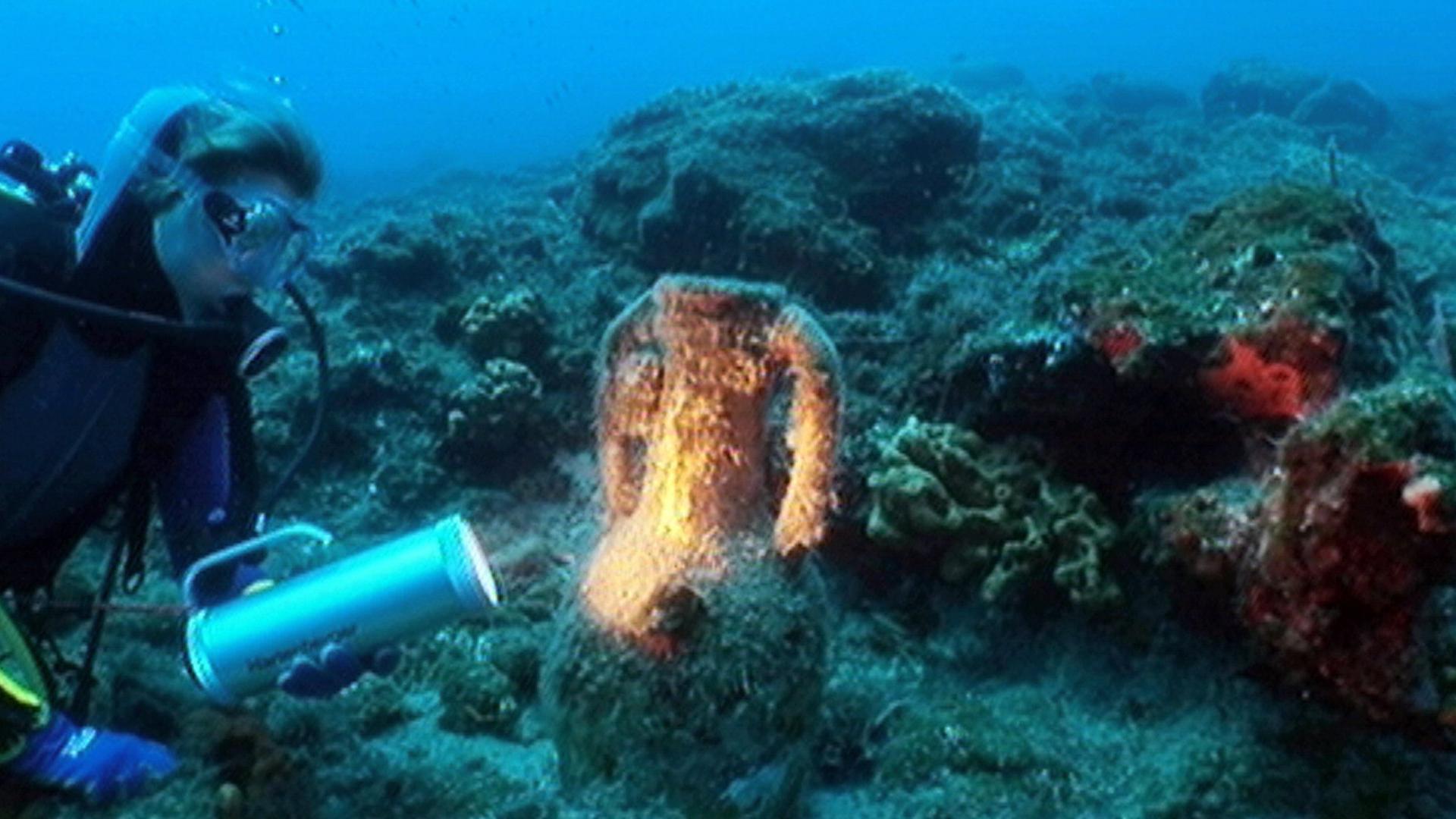 Ein Taucher leuchtet eine alte Amphore am Meeresgrund an.