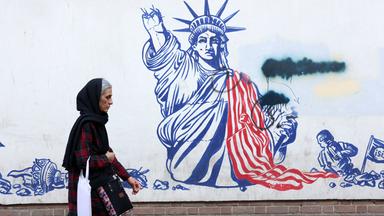Frau mit Kopftuch geht an einem Wandbild vorbei. Darauf ist die Freiheitsstatue mit abgefetztem Arm zu sehen.