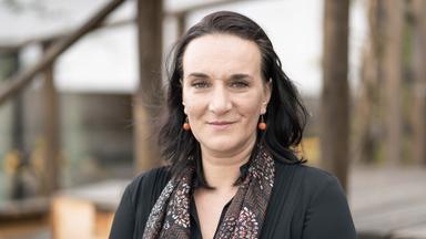 Frau mit langen schwarzen Haaren und roten kugelförmigen Ohrringen.