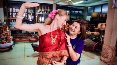Eine blonde Frau in traditionellem Gewand und eine thailändische Frau, die den Arm um ihre Schultern gelegt hat.