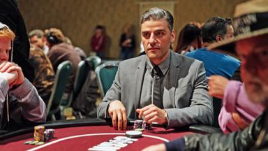 William Tell (Oscar Isaac) sitzt in einem grauen Anzug und Krawatte an einem Pokertisch. Vor ihm liegen zwei Stapel Chips und er schaut konzentriert nach vorn. Um ihn herum sind verschwommen weitere Spieler zu sehen.