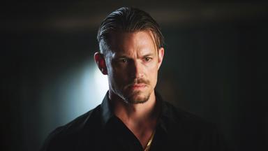 Pete Koslow (Joel Kinnaman) steht mit ernstem Gesichtsausdruck in einem dunklen Raum.