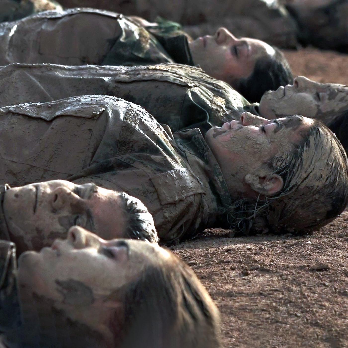 Einige Frauen in Militärkleidung liegen schlammbeschmiert und geschlossenen Augen nebeneinader auf dem Boden