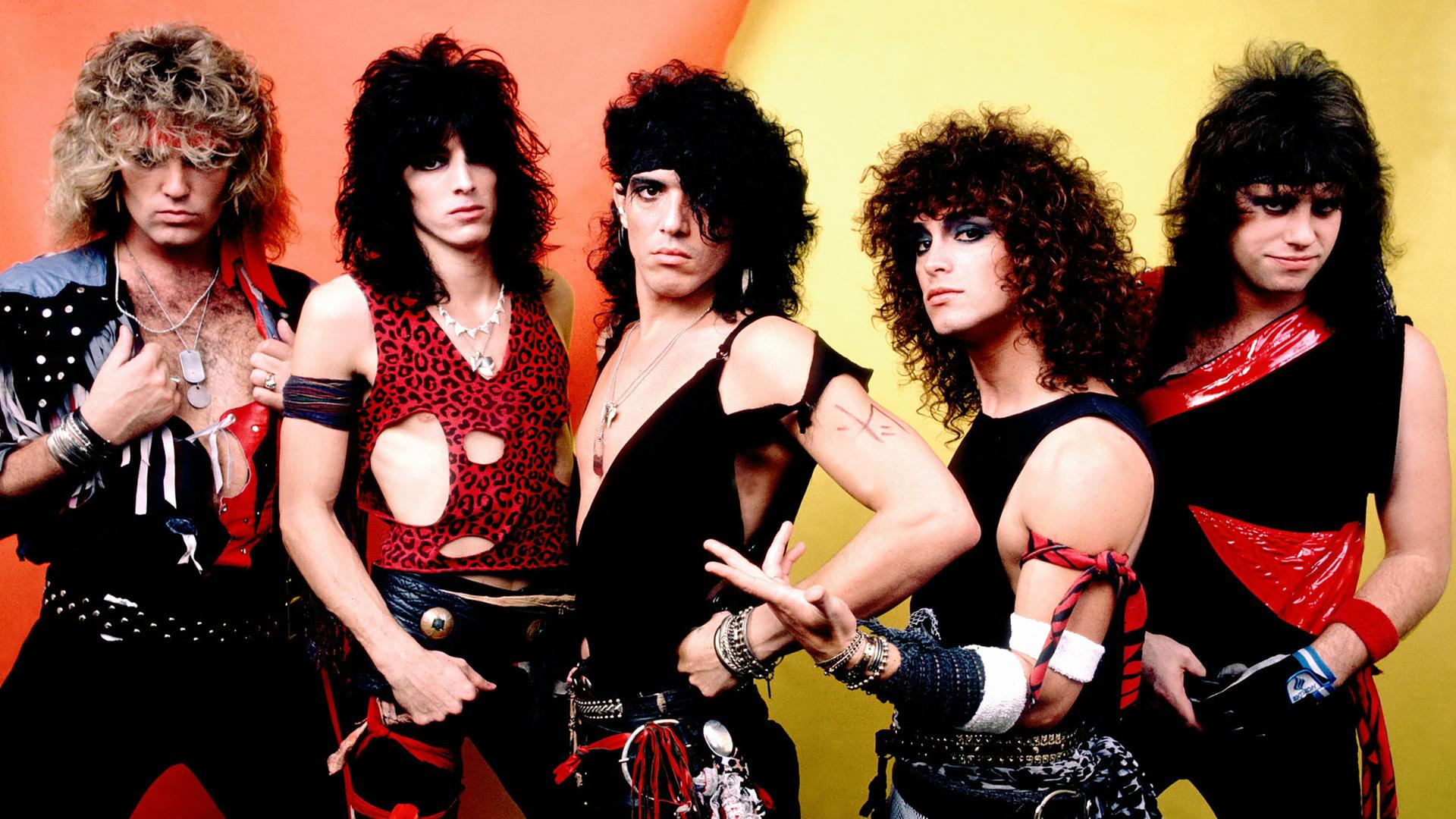 Die Bandmitglieder von "Ratt" mit toupierten Haaren und teils zerrissener Kleidung posieren vor der Kamera.