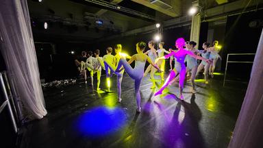 Junge Balletttänzerinnen tanzen auf einer Bühne in einem dunklen Raum aus Beton.