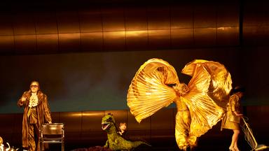 4 Schauspieler*innen auf einer Bühne. Eine wirbelt einen goldenen Mantel in die Luft.