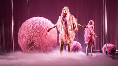 Bühnenszene: Zwei Personen mit rosa-farbenen Kostümen stehen zwischen großen rosa-farbenen Kugeln.