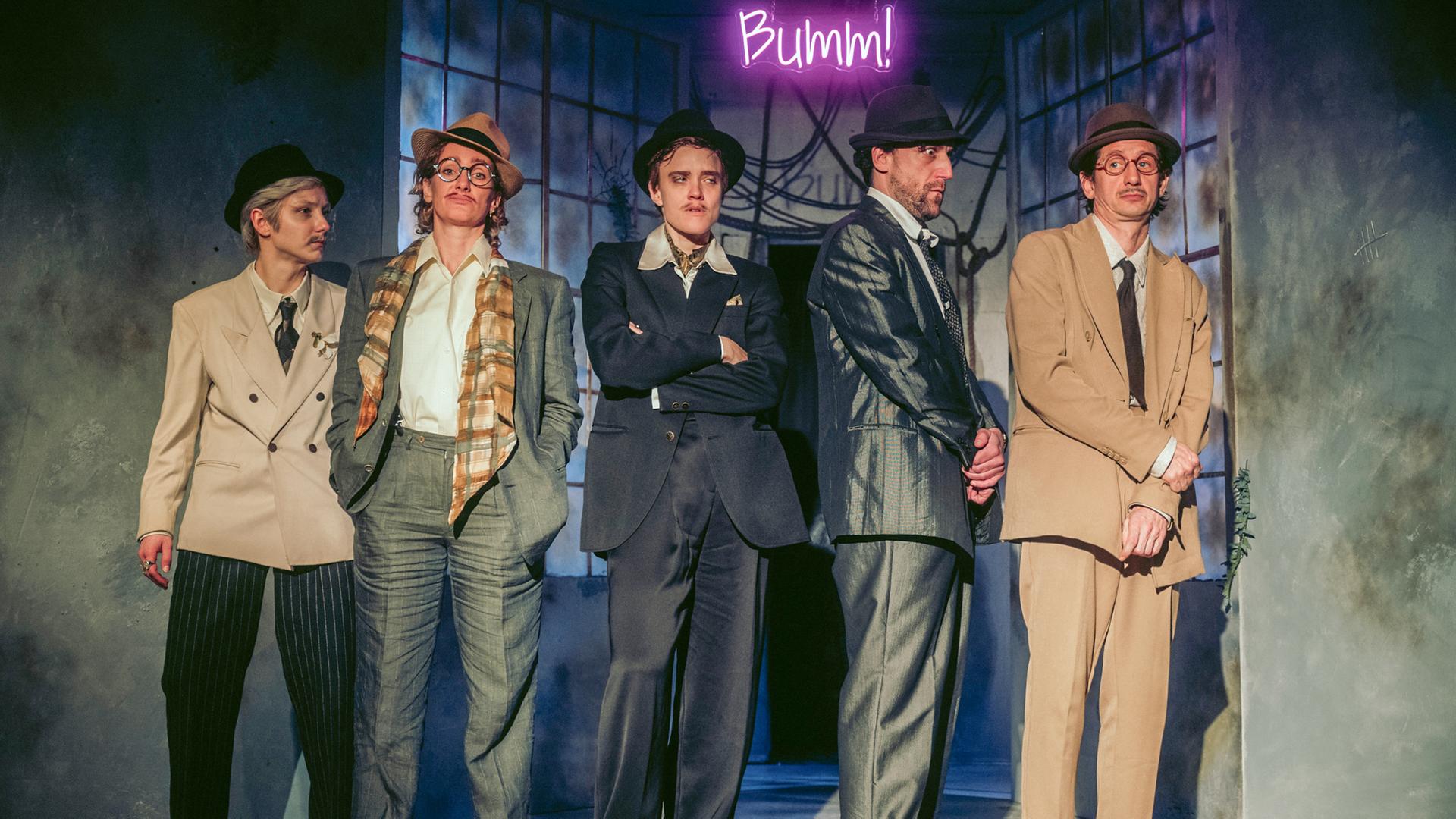 Fünf Personen mit Anzügen und Hüten bekleidet stehen auf der Bühne.