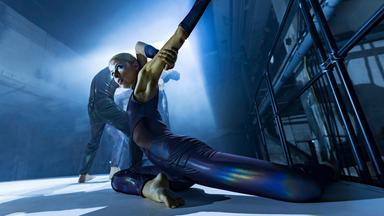 Tänzer und Tänzerinnen, die futuristische Kostüme tragen tanzenauf einer Bühne.