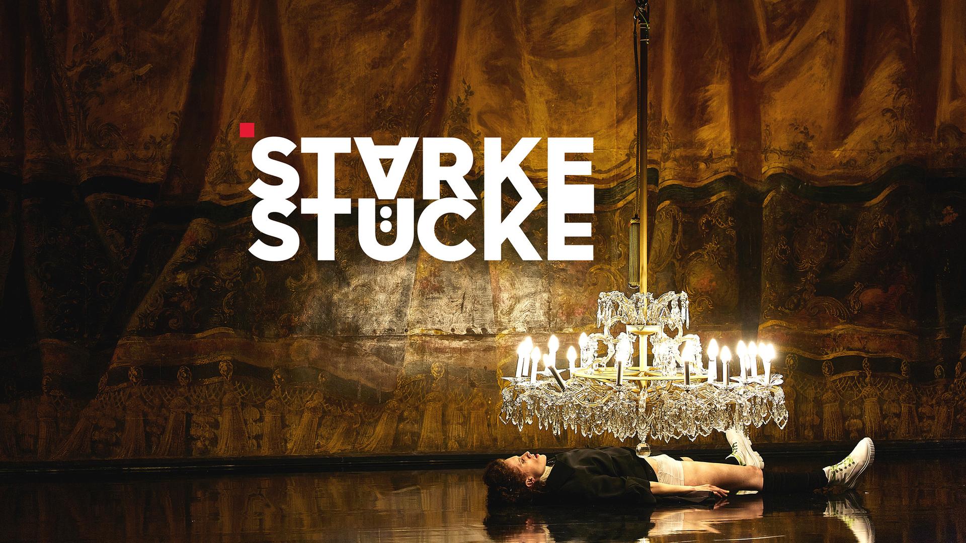 Teaser mit Logo Theatertreffen Starke Stücke - Eine Frau liegt ausgestreckt auf dem Rücken auf einem hochglänzenden, schwarzen Bühnenboden. Direkt über ihrem Oberkörper hängt ein großer Kristalllüster mit vielen brennenden Kerzen, deren Licht sich auf der Bodenfläche spiegelt. Im Hintergrund hängt ein Bühnenvorhang in warmen Braun‑ und Goldtönen