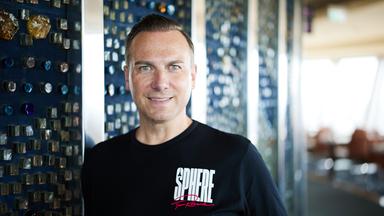 Porträtfoto eines Mannes mit ganz kurzen mittelblonden Haaren und blauen Augen, der ein schwarzes T-Shirt mit der weißen Aufschrift Sphere trägt.