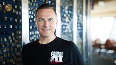 Porträtfoto eines Mannes mit ganz kurzen mittelblonden Haaren und blauen Augen, der ein schwarzes T-Shirt mit der weißen Aufschrift Sphere trägt.