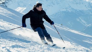Andréas fährt auf Skiern einen Hang im verschneiten Gebirge hinab.
