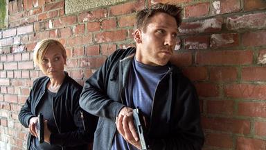 "Tod im Internat (1)": Isabell Mosbach alias Karla Parker (Nadja Uhl) und ihr Kollege Sellinger (Hanno Koffler) stehen mit Pistolen im Anschlag vor einer Wand und suchen Deckung.