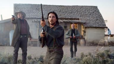 Dan Evans (Christian Bale) hält schussbereit ein Gewehr im Anschlag und schaut konzentriert und angespannt. An seiner rechten Seite, einige Schritte zurück, steht Tucker (Kevin Durand) mit ausgestrecktem rechten Arm und zielt mit seinem Revolver. Im Hintergrund seitlich links hinter den beiden kommt Byron McElroy (Peter Fonda) angelaufen, er hält ein Gewehr mit sehr kurzem Lauf in Händen.