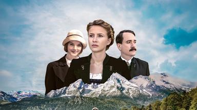 Die Abbildung zeigt eine malerische Landschaft mit Bergen im Hintergrund. Im Vordergrund trägt eine junge Frau mit einem Koffer ein traditionelles Kleid. Hinter ihr sind zwei Personen in historischen Kleidern zu sehen.