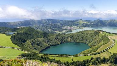 Blick über die grüne Vulkanlandschaft von Sete Cidades auf São Miguel. Mehrere Kraterseen liegen zwischen bewaldeten Hügeln und steilen Berghängen.