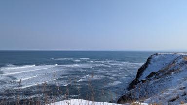 Winterlicher Blick auf Kap Shiretoko auf Hokkaidō mit schneebedeckten Klippen und dem blauen Meer vor der Küste.