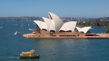 Panoramabild des Opernhauses von Sydney. Auf dem Wasser rund um das Gebäude sind mehrere Boote zu erkennen