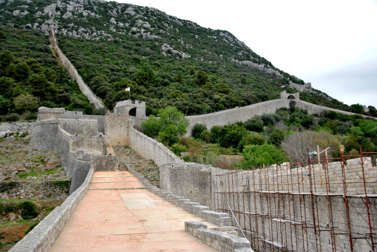 Steinerne Festungsanlagen und Mauern, die sich kreuz und quer über einen bewaldeten Hügel ziehen.