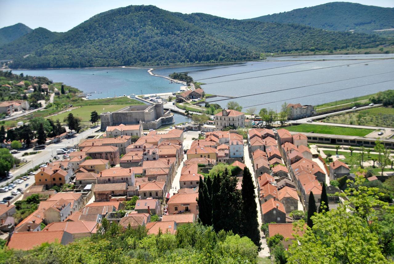 Blick über ein Dorf mit roten Ziegeldächern - im Hintergrund eine Meereslagune mit Absperrungen zur Salzgewinnung