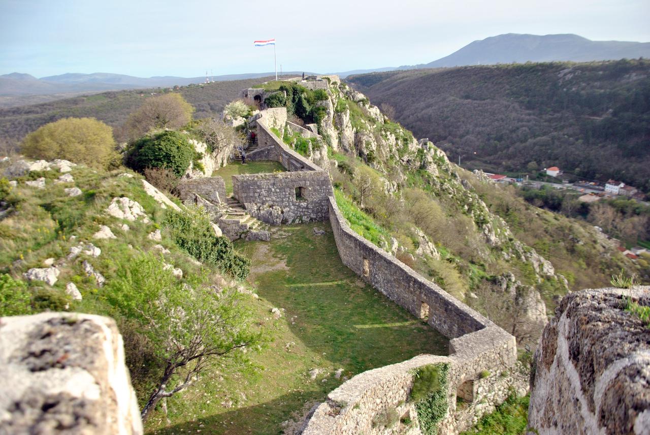 Überreste einer langgezogenen Festungsanlage auf einem Felsen, nur die Außenmauern stehen noch