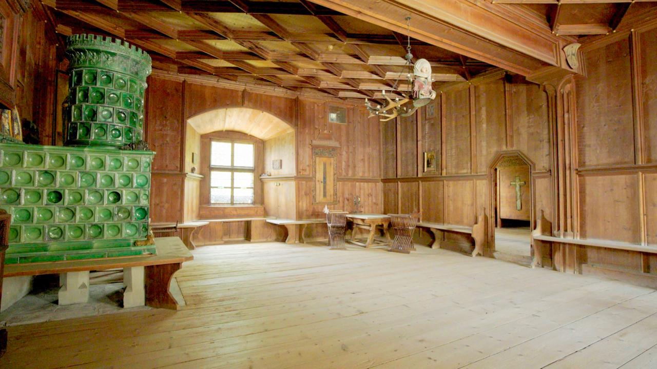 Ein historischer Raum mit Holzwänden, Holzmöbeln und einem großen grünen Kachelofen.