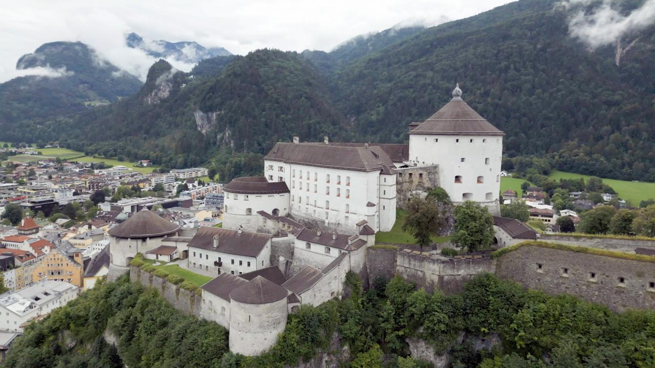 Luftaufnahme einer Festung über dem Ort Kufstein, umgeben von grünen Wäldern.