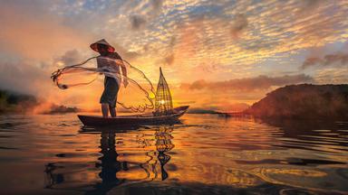 Ein Fischer in einem kleinen Boot wirft bei Sonnenaufgang sein Netz aus.