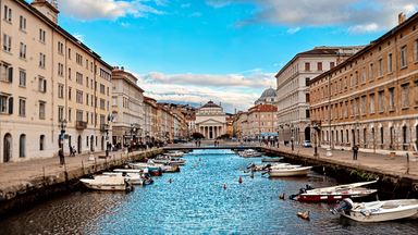 Blick entlang des Canale Grande in Triest mit Booten, historischen Gebäuden und einer Kirche im Hintergrund.